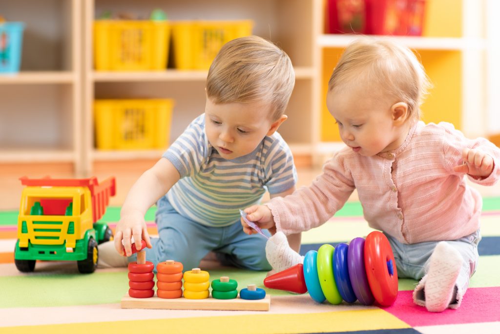 Close-up of a baby boy and girl playing with toys together on the floor