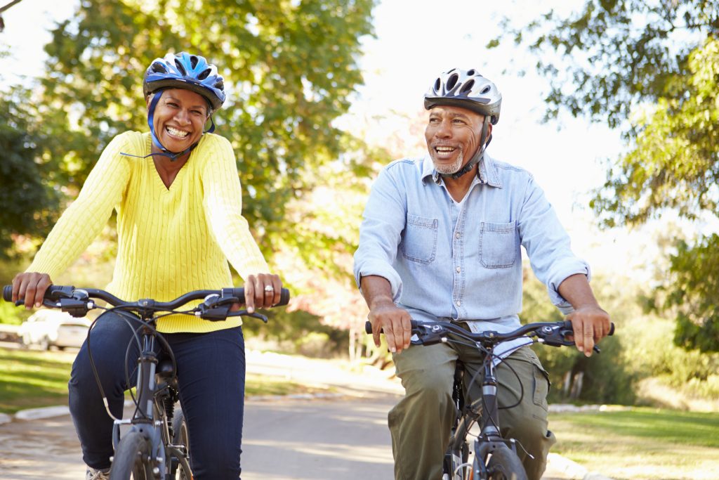 Two older adults smiling and wearing helmets while biking on a path